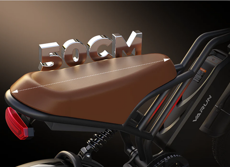 A close-up of a brown bicycle seat with a metallic 50CM sign above it, indicating its length. The bike frame, rear light, and part of the Varun logo are also visible.