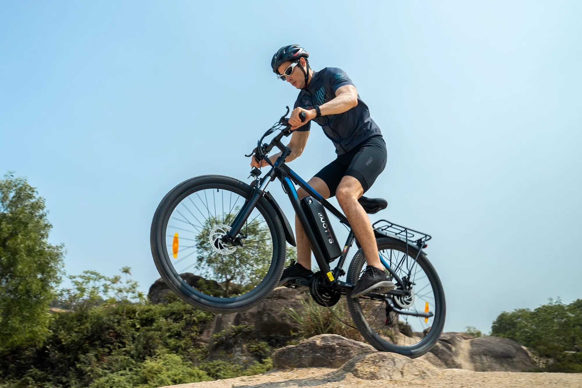 Man wearing helmet and sunglasses riding an electric mountain bike over rocky terrain outdoors under clear sky