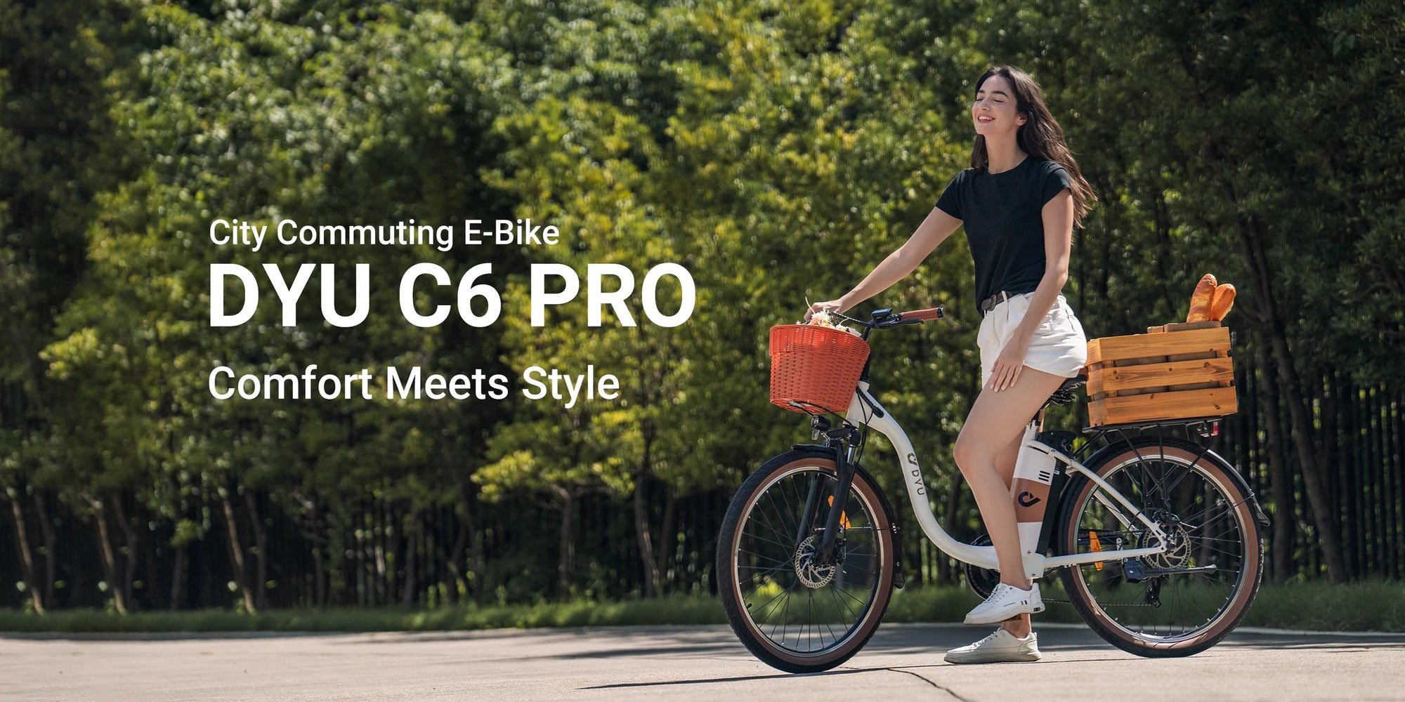 A woman in a black shirt and white shorts smiles while riding a DYU C6 PRO e-bike with a front basket and wooden rear rack on a sunny street with trees in the background. Text reads: “City Commuting E-Bike DYU C6 PRO Comfort Meets Style.”.