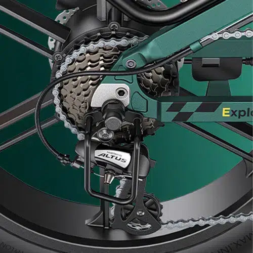 Close-up of a bicycle’s rear gear mechanism, showing the Shimano Altus derailleur, cassette, chain, and part of the green bike frame against a teal background.