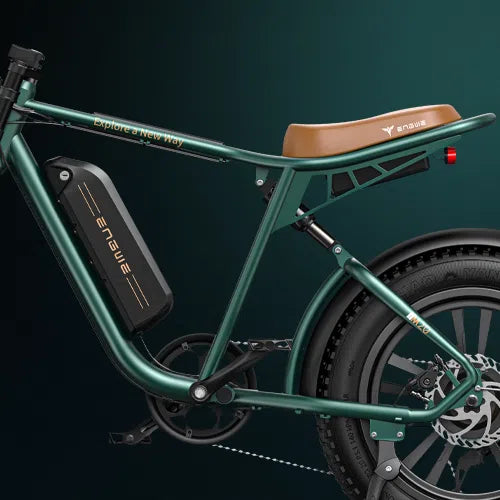 Close-up view of a green electric bicycle with a brown seat, battery pack on the frame, and thick rear tire against a dark green background. The frame has the text Explore a New Way printed on it.