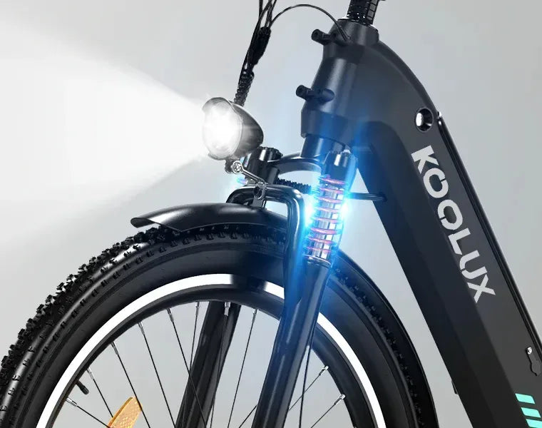Close-up of the front wheel and suspension of a black KOOLUX electric bike, with an illuminated headlight and a glowing blue light near the fork, highlighting the bikes sturdy design and modern features.