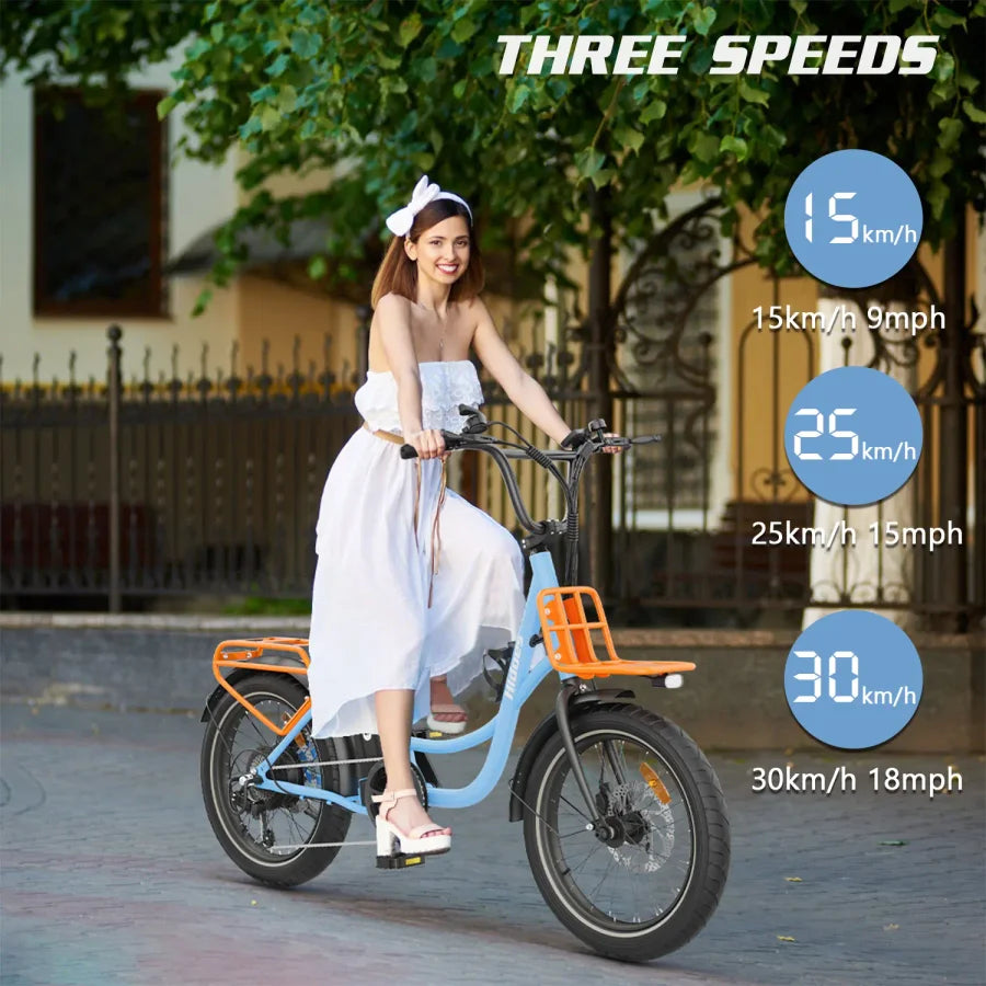 A woman in a white dress and headband rides a blue electric bicycle with orange racks. Text on the image highlights three speed options: 15 km/h (9 mph), 25 km/h (15 mph), and 30 km/h (18 mph).