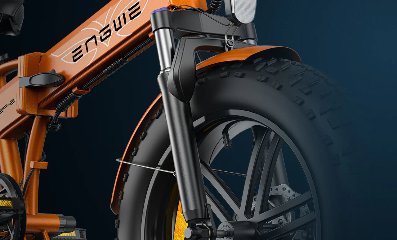 Close-up of the front wheel and suspension fork of an orange electric bike, displaying thick, rugged tires, and part of the bike frame with the word ENGWE visible. The background is dark blue.