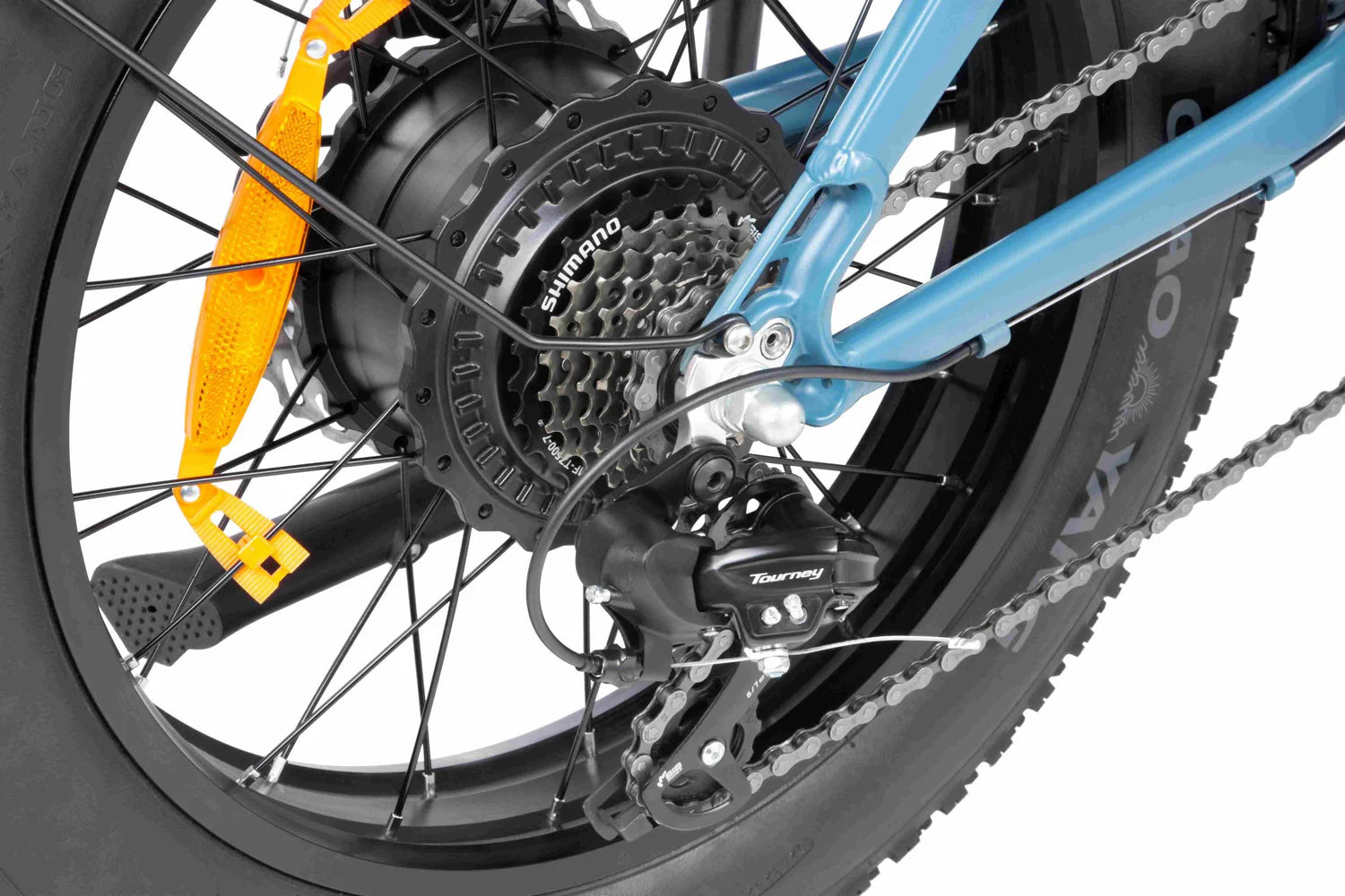 Close-up of a bicycle’s rear wheel showing the Shimano gear cassette, derailleur, chain, black spokes, tire tread, and an orange reflector attached to the frame.