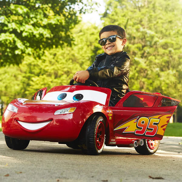Young boy wearing sunglasses and a black jacket sitting in a red toy car designed like a race car on a driveway