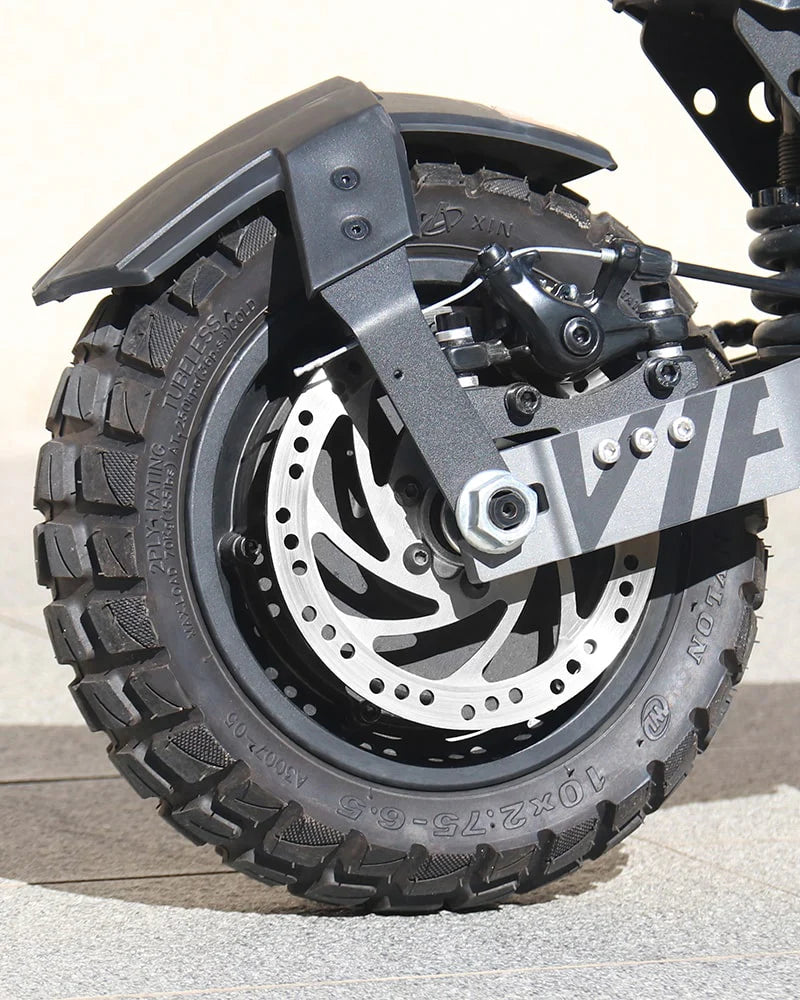 Close-up of the Vipcoo VS6 1000W Electric Scooter’s rugged, deep-tread all-terrain tire on a metal wheel, featuring a large disc brake and partially covered by a black fender.