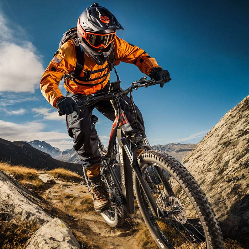 A mountain biker in orange gear rides the Randride YX90A Electric Mountain Bike by Randride down a rocky mountain trail beneath a blue sky.