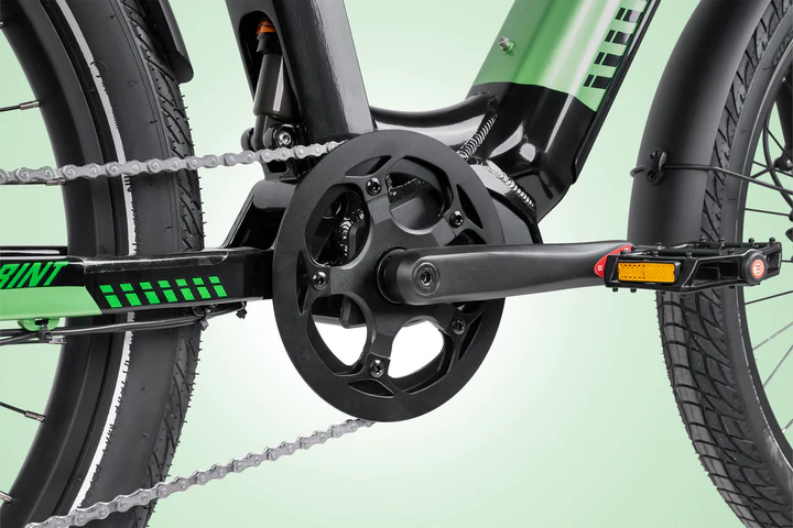Close-up of a bicycles drivetrain showing the black crankset, chain, and pedals attached to a green and black bike frame with thick tires against a light green background.