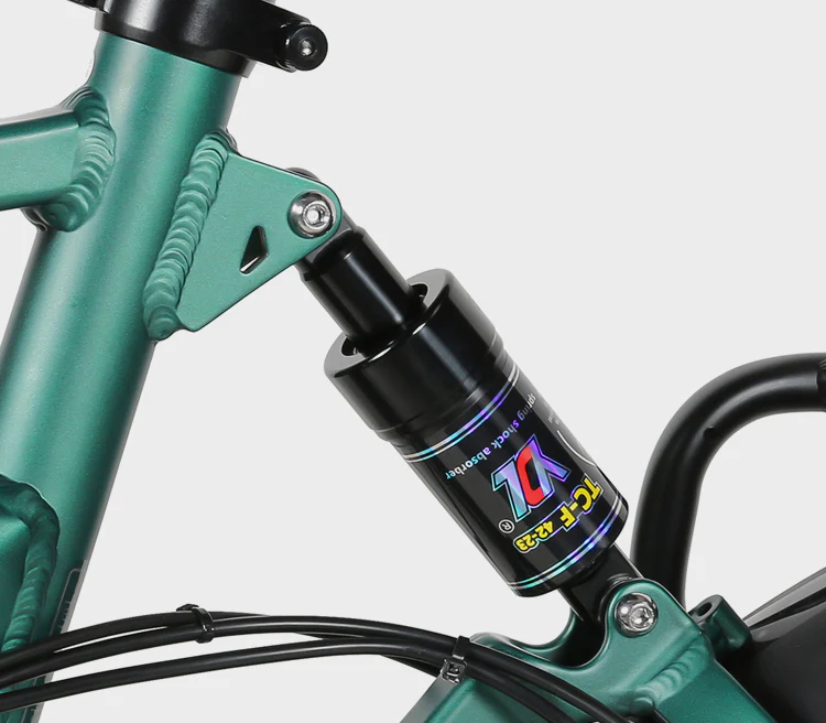 Close-up of a teal bicycle frame featuring a black rear suspension shock absorber with colorful branding and visible mounting bolts. Black cables are also seen running along the frame.