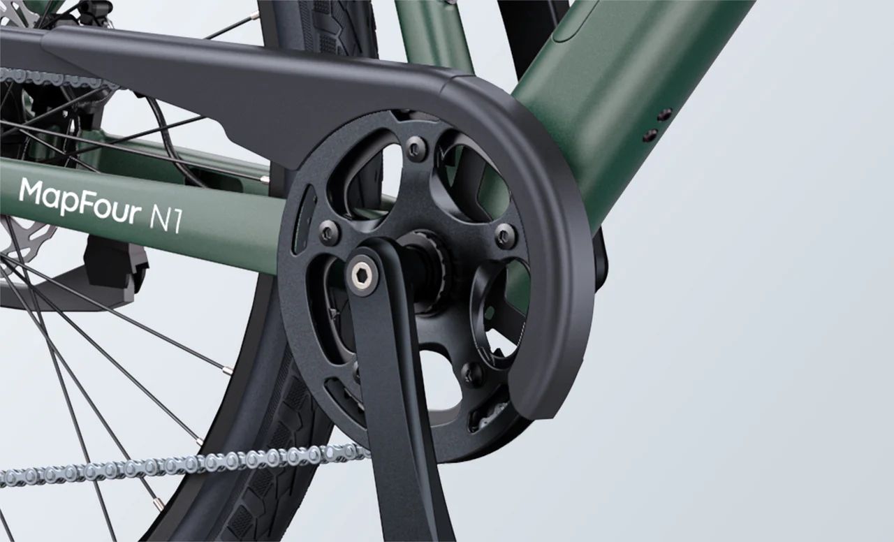 Close-up view of a bicycle crankset and chainring with a protective guard, featuring a green frame labeled MapFour N1 and a visible segment of the rear wheel and chain.