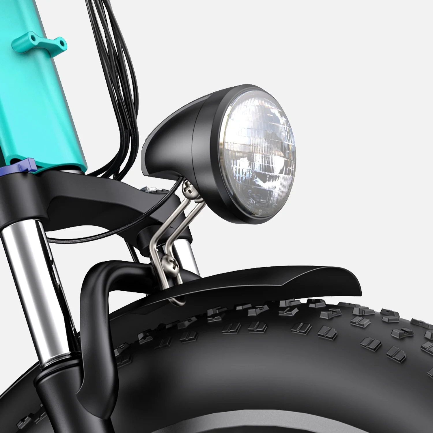 Close-up view of a bicycle’s front headlight mounted above a thick, knobby tire and black fender, with part of the bike frame and cables visible in the background.