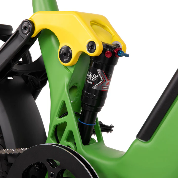 Close-up of a green and yellow bicycle frame featuring a black DNM shock absorber and part of the black crankset, highlighting the suspension system.
