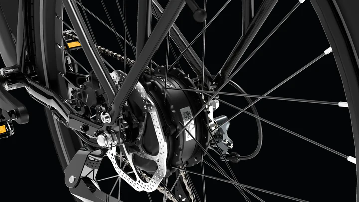 Close-up view of a bicycle’s rear wheel showing spokes, disc brake rotor, gear cassette, derailleur, and a hub motor, all set against a black background.