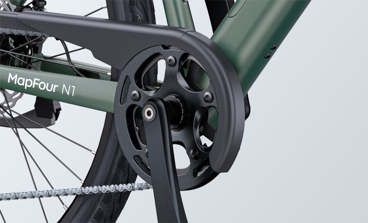 Close-up view of a green bicycle’s crankset, chain guard, and pedal, with part of the rear wheel and chain visible. The frame has the text “MapFour N1” printed on it.